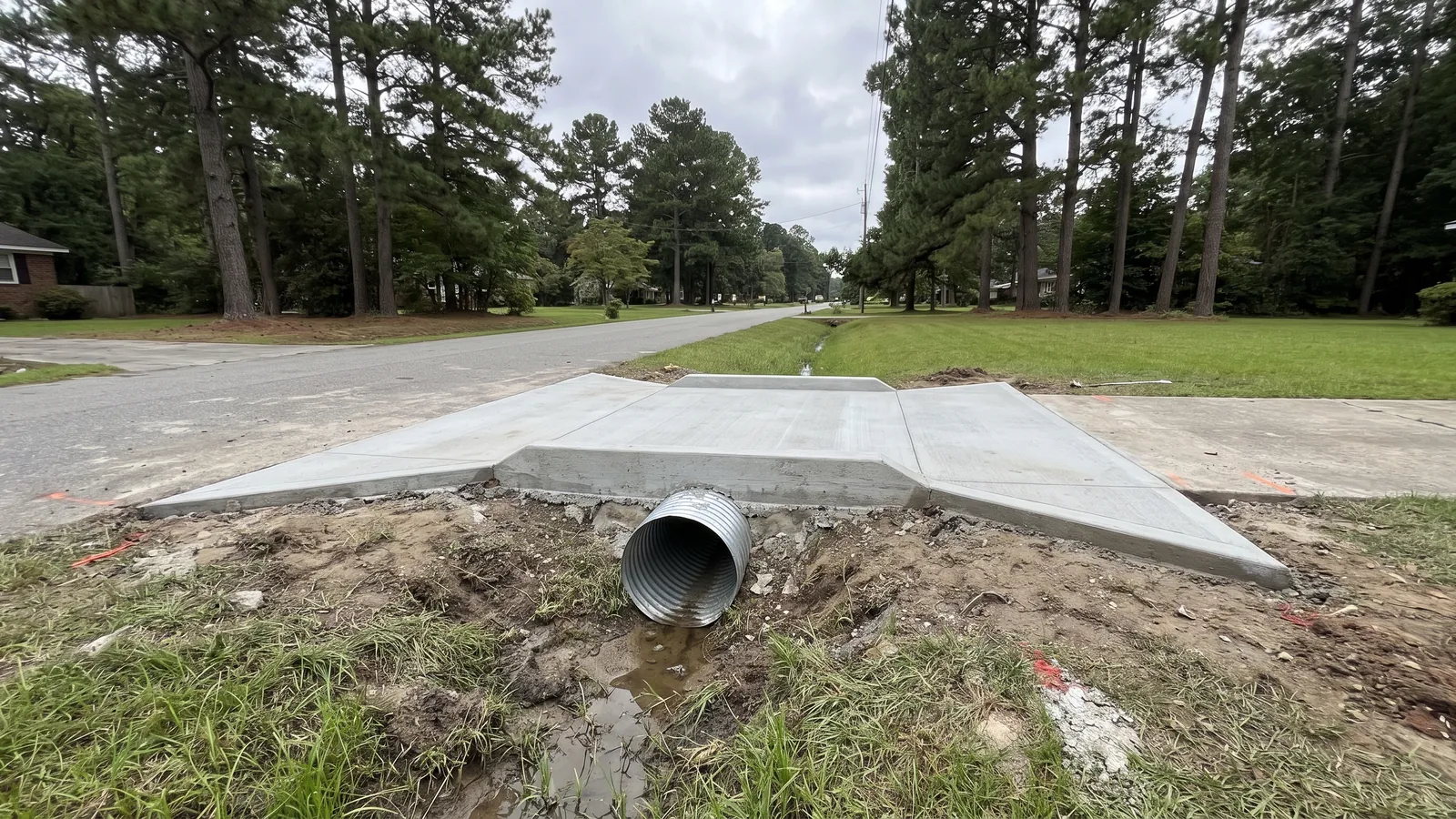 New concrete driveway apron crossing a grassy roadside swale on a culvert pipe with poured end sections on a pine-lined Dorchester County street